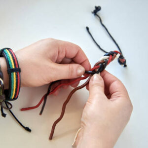 Woman's hands making a leather bracelet on a white background, close-up.
